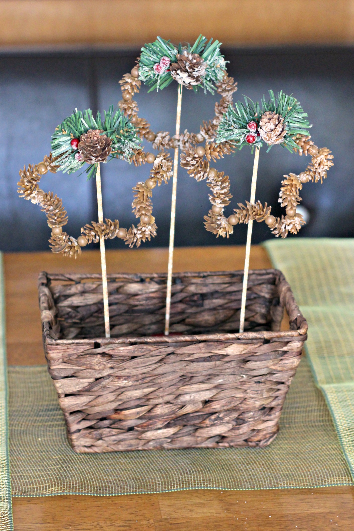 Three dollar store pinecone snowflake ornaments on washi tape wrapped skewers standing in a small dark woven basket